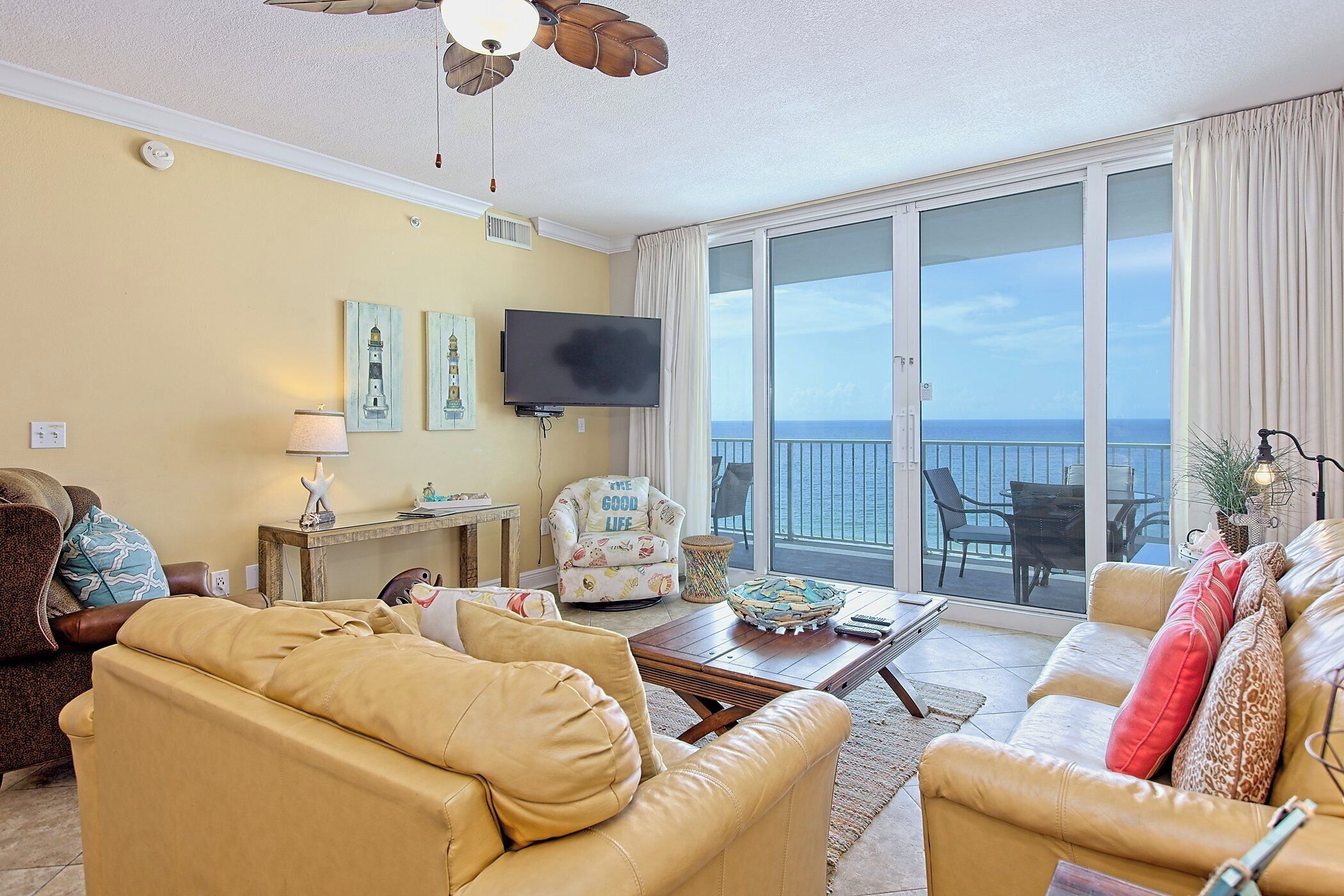 Ein Wohnzimmer mit einer Couch, einem Sessel und einem Flachbildfernseher. Ein Balkon bietet Blick auf den Ozean.