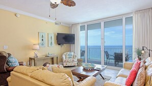 A living room with a sofa, armchair, and a flat-screen TV. There is a balcony with a view of the ocean. - San Carlos #605 by Southern Vacation Rentals (Gulf Shores)