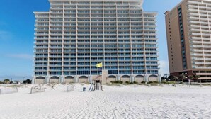 A large hotel with multiple floors and balconies, situated on a sandy beach with clear skies. - San Carlos #605 by Southern Vacation Rentals (Gulf Shores)