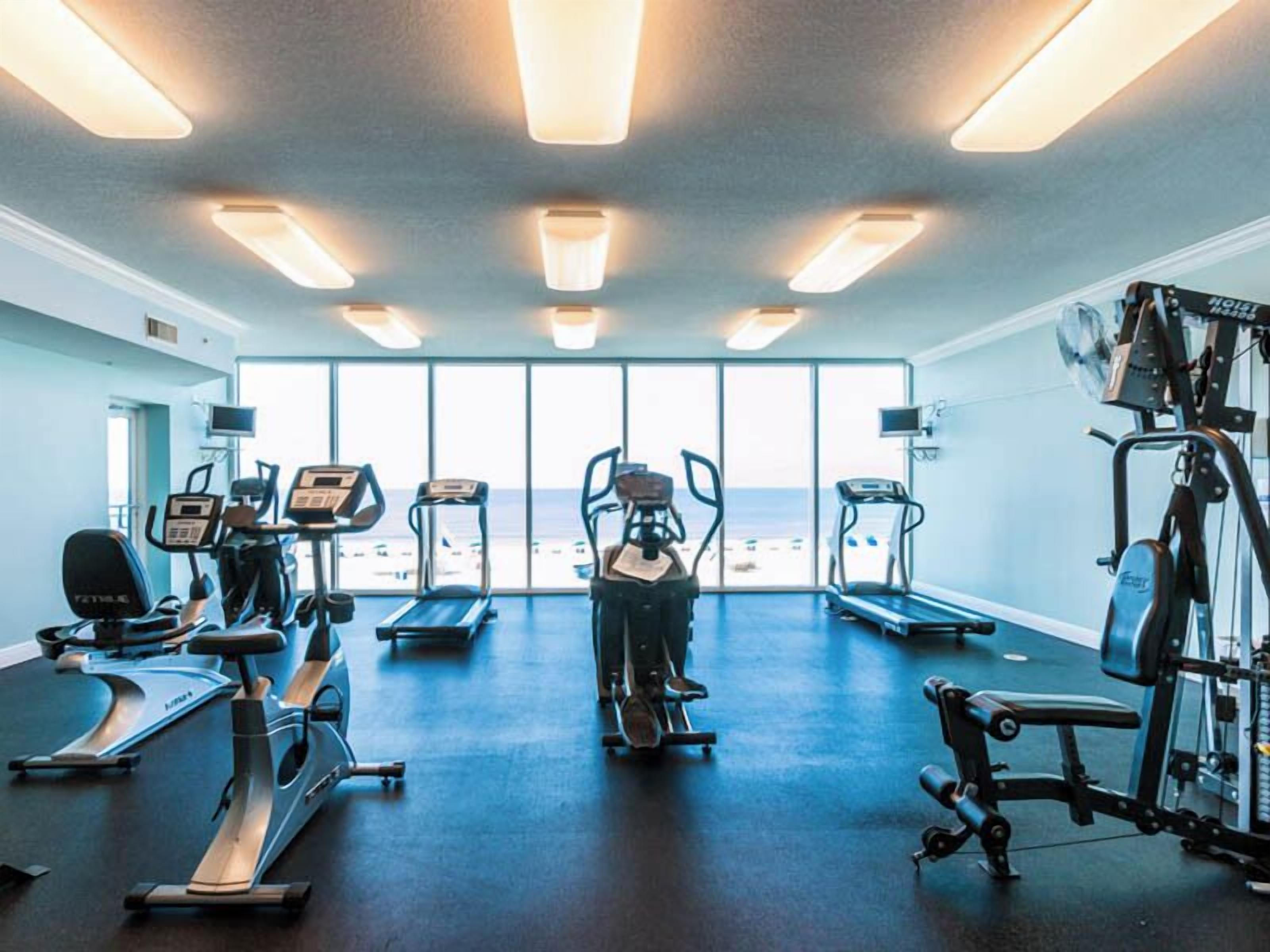 A gym with cardio machines, weight equipment, and large windows offering a view of the beach.