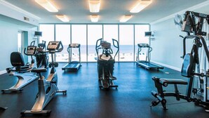 A gym with cardio machines, weight equipment, and large windows offering a view of the beach. - San Carlos #605 by Southern Vacation Rentals (Gulf Shores)
