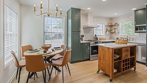 A modern kitchen with a central island, built-in appliances, and a dining area with chairs and a table.