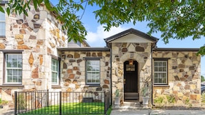 A stone house with a well-maintained lawn and a black metal fence.
