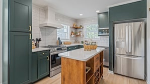 A modern kitchen with dark green cabinets, stainless steel appliances, and a central island.