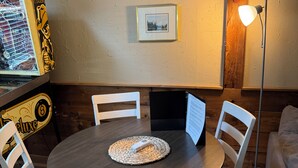 A dining area with a round table, white chairs, a woven placemat, a framed picture on the wall, and a floor lamp. - Welcome to “The Pines” at The Cedars (Cultus Lake)