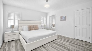 Ein Schlafzimmer mit einem großen Bett, einem Nachttisch, einem Schminktisch, einem Spiegel und einer Tür.