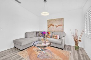 Uma sala de estar moderna com um sofá modular cinzento, uma mesa de centro de vidro e um quadro na parede.