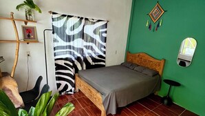 Une chambre à coucher avec un lit, un ventilateur de plafond, un mur vert, une fenêtre avec un miroir et une plante en pot.