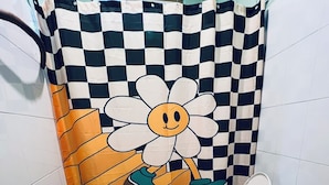 Une salle de bain avec un rideau de douche à carreaux orné d’un grand motif floral, des toilettes et un sol carrelé.