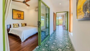 A bedroom with a bed, a ceiling fan, and a glass door leading to a hallway with patterned flooring.