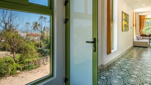 A hallway with a large window, patterned floor, and a door leading to a room with a view of greenery and buildings.