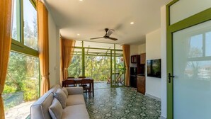 A room with a sofa, dining table, and chairs, a ceiling fan, and large windows with curtains.