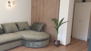 A sectional sofa with multiple cushions, a potted plant, a wooden slat wall, and a white cabinet. - Panorama Suite Waldhaus 3-bedroom apartment near Obereggen directly hiking trail (Nova Ponente)
