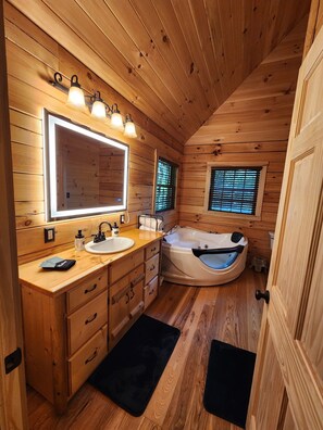 Ein Badezimmer einer Holzhütte mit einem großen Spiegel, zwei Waschbecken, einer Badewanne und einem Fenster mit Jalousien.