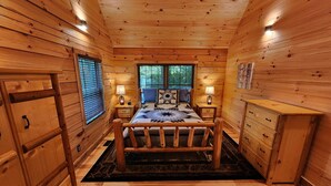 A wooden cabin bedroom with a bed, nightstands, a dresser, and a window with blinds.