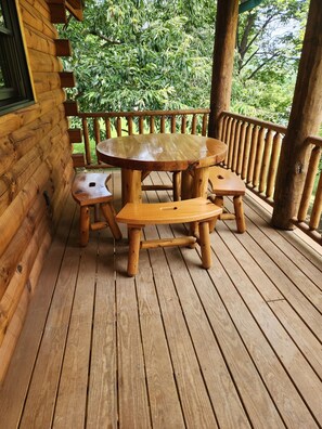 Eine Holzterrasse mit einem runden Tisch und Bänken, umgeben von einem Holgitter.
