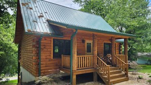 A log cabin with a porch, wooden steps, and a metal roof.