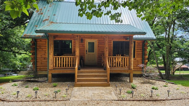 A wooden cabin with a porch, a front door, and a metal roof.