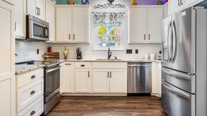 A modern kitchen with white cabinets, stainless steel appliances, and a wooden floor. - Southern Charm by Southern Vacation Rentals (Foley)
