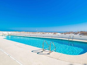 A rectangular swimming pool with a white deck and metal ladders, surrounded by a white fence and a clear blue sky. - Summerchase #202 by Southern Vacation Rentals (Orange Beach)