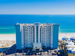 Un hôtel de grande hauteur doté d’un atrium central, situé près d’une plage aux eaux d’un bleu limpide.