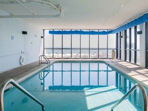 Une piscine intérieure offrant une vue dégagée sur la plage grâce à de grandes fenêtres.