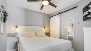 A bedroom with a large bed, bedside lamps, a ceiling fan, a window with a plant, and a sliding door closet. - Sunrise Village #210 by Southern Vacation Rentals (Gulf Shores)