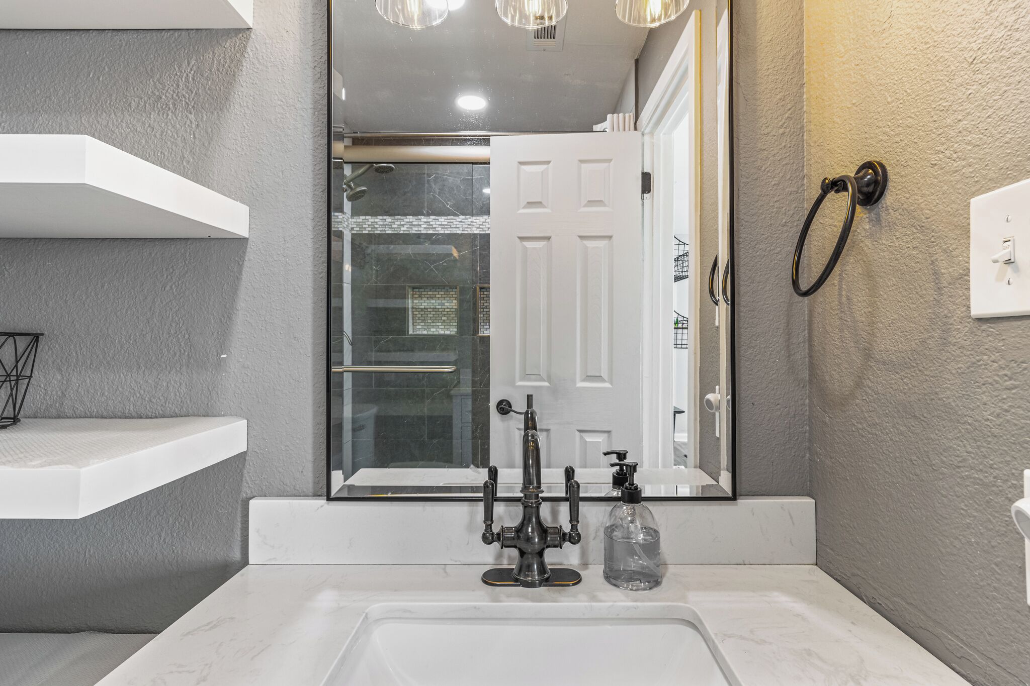 A bathroom with a white sink, a mirror, a shower, and a towel ring.