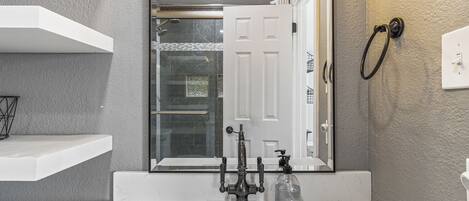A bathroom with a white sink, a mirror, a shower, and a towel ring.