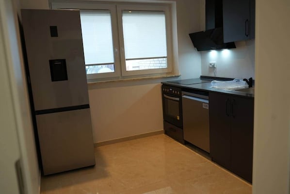 A compact kitchen with a refrigerator, oven, and cabinets, a window with blinds, and a tiled floor. - Modern Apartment | Balcony | 2 Bedrooms | Parking Space (Garbsen)