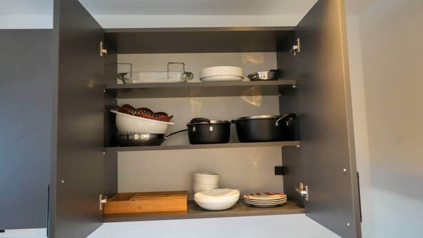 Un mueble abierto con estantes que contienen utensilios de cocina, incluyendo ollas, sartenes y platos.