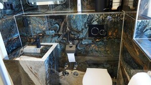 Un baño con salpicadero de mármol, inodoro, lavabo con grifo y zona de ducha.