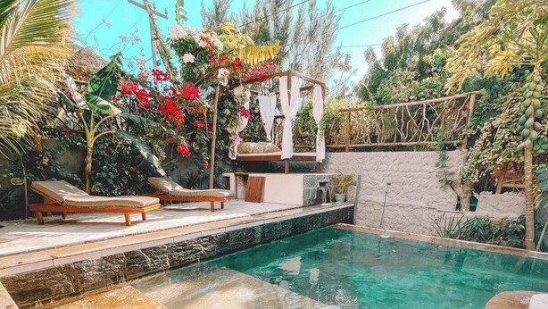 Une piscine dotée d’une terrasse en pierre, entourée d’une végétation luxuriante et agrémentée d’un petit espace détente avec des coussins.