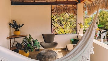 A hammock in a room with a thatched roof, a window with a view of greenery, and several potted plants.