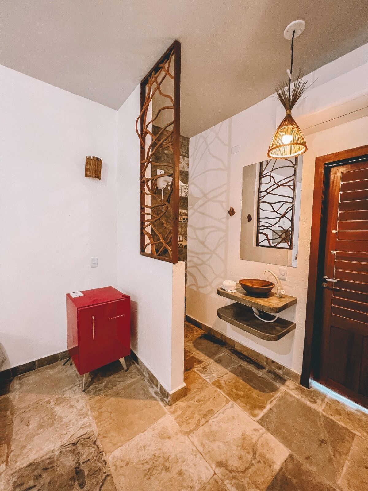 Un couloir avec un meuble rouge, un panneau décoratif mural, un lavabo avec un receveur et une porte en bois.