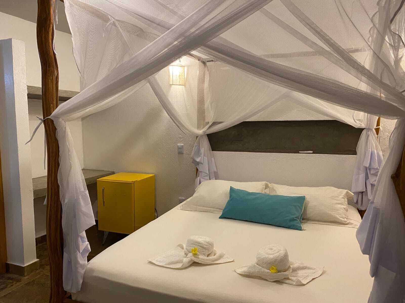 Ein Bett mit Baldachin, ein Nachttisch und ein gelbes Schränkchen.