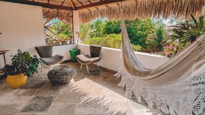 Une terrasse couverte avec un toit de chaume, un sol en pierre et du mobilier d’extérieur.