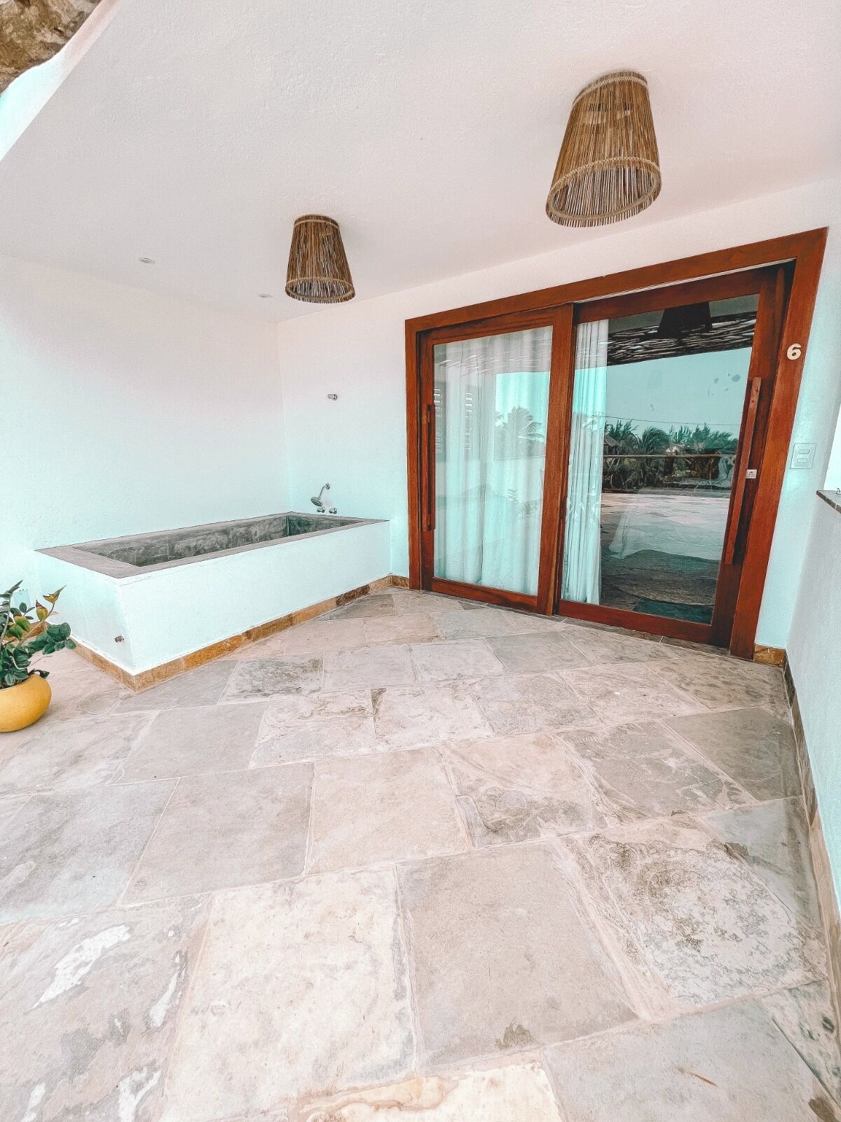 Un balcón con suelo de piedra, una bañera integrada y una puerta de cristal que da a un jardín.