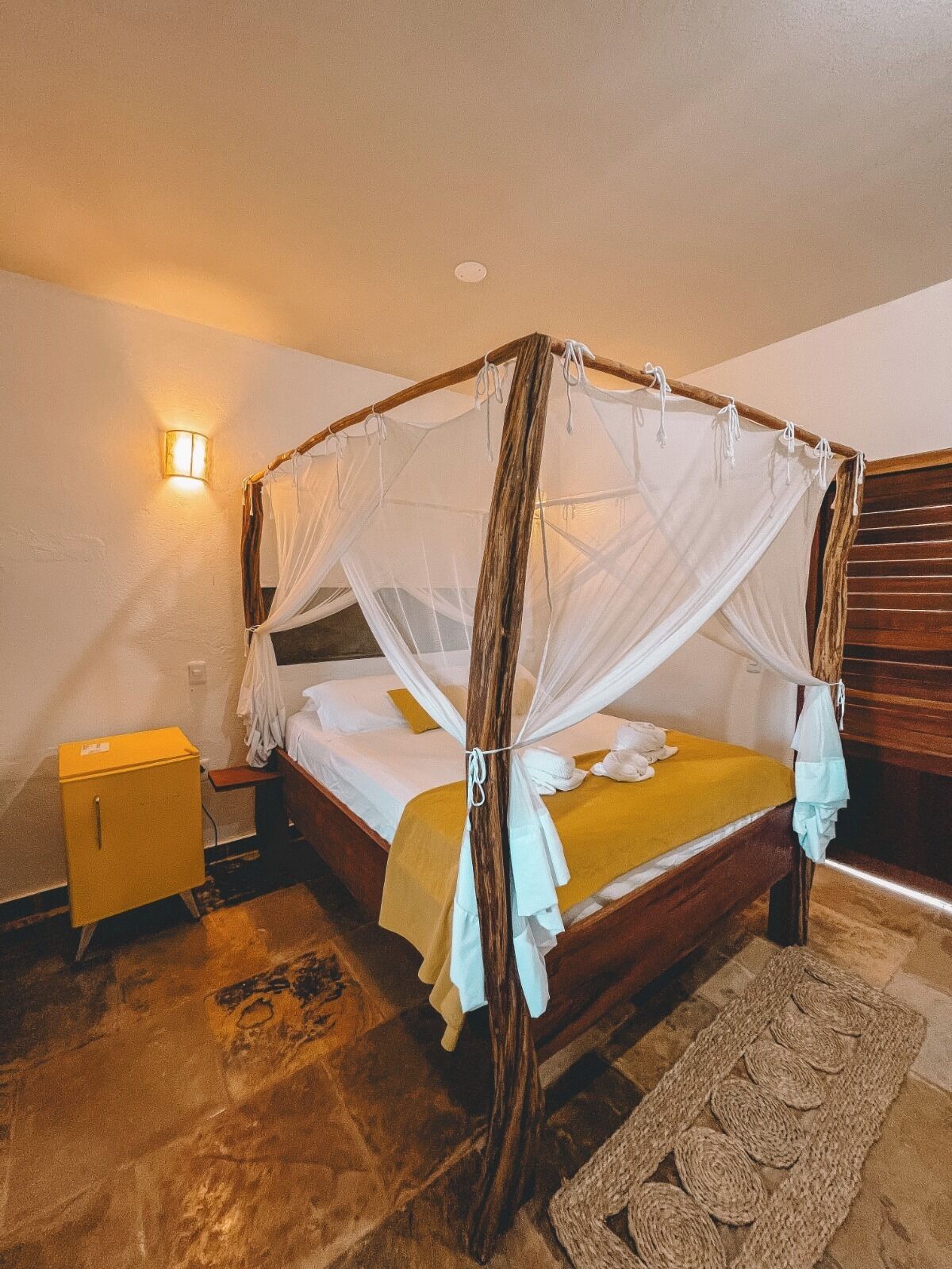 Ein Himmelbett mit Baldachin, ein Nachttisch, eine Wandleuchte und ein gewebter Teppich.