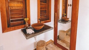 Une salle de bain avec un meuble-lavabo en bois, un grand miroir et un sol carrelé en pierre.