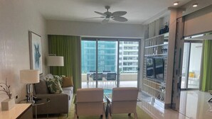 A modern living room with a sofa, two armchairs, a coffee table, a TV, and a balcony with a view of buildings. - Chic 1-bdr resort in fabulous Cancun. (Puerto Vallarta)