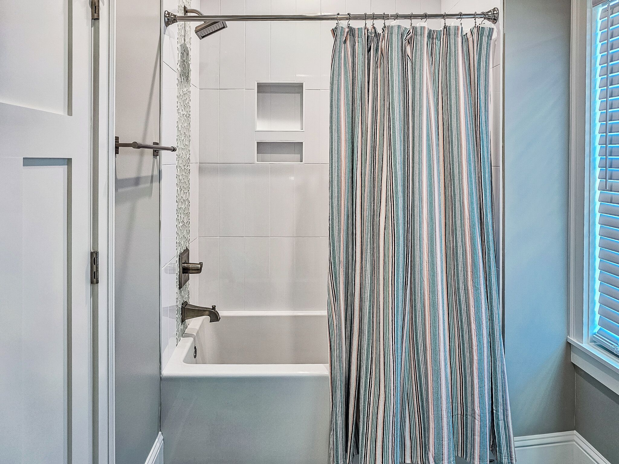 Een badkamer met een bad, douchegordijn en een raam met zonwering.