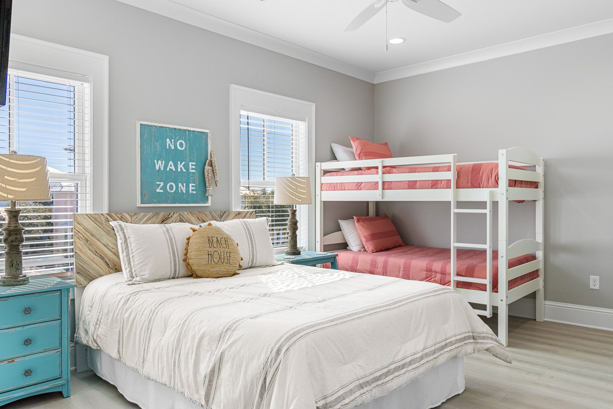 A bedroom with a bunk bed, a bed with multiple pillows, a nightstand, and a wall sign.