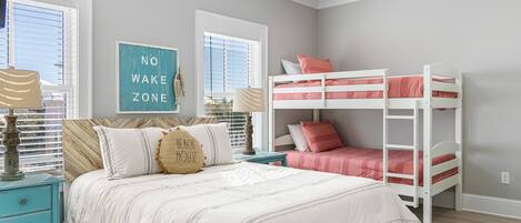 A bedroom with a bunk bed, a bed with multiple pillows, a nightstand, and a wall sign.