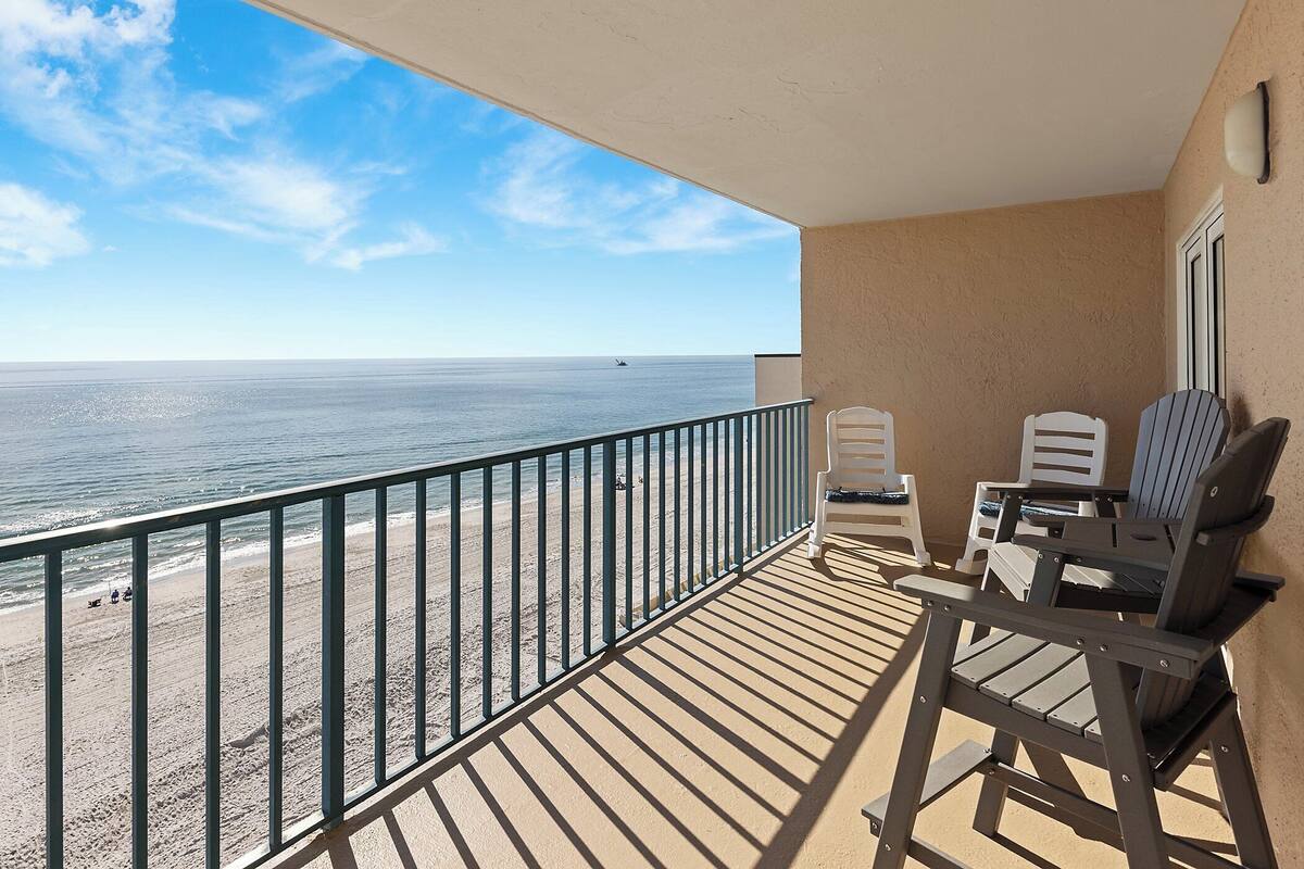 Ein Balkon mit Blick auf Strand und Meer. Zwei Stühle und ein Tisch sind vorhanden.