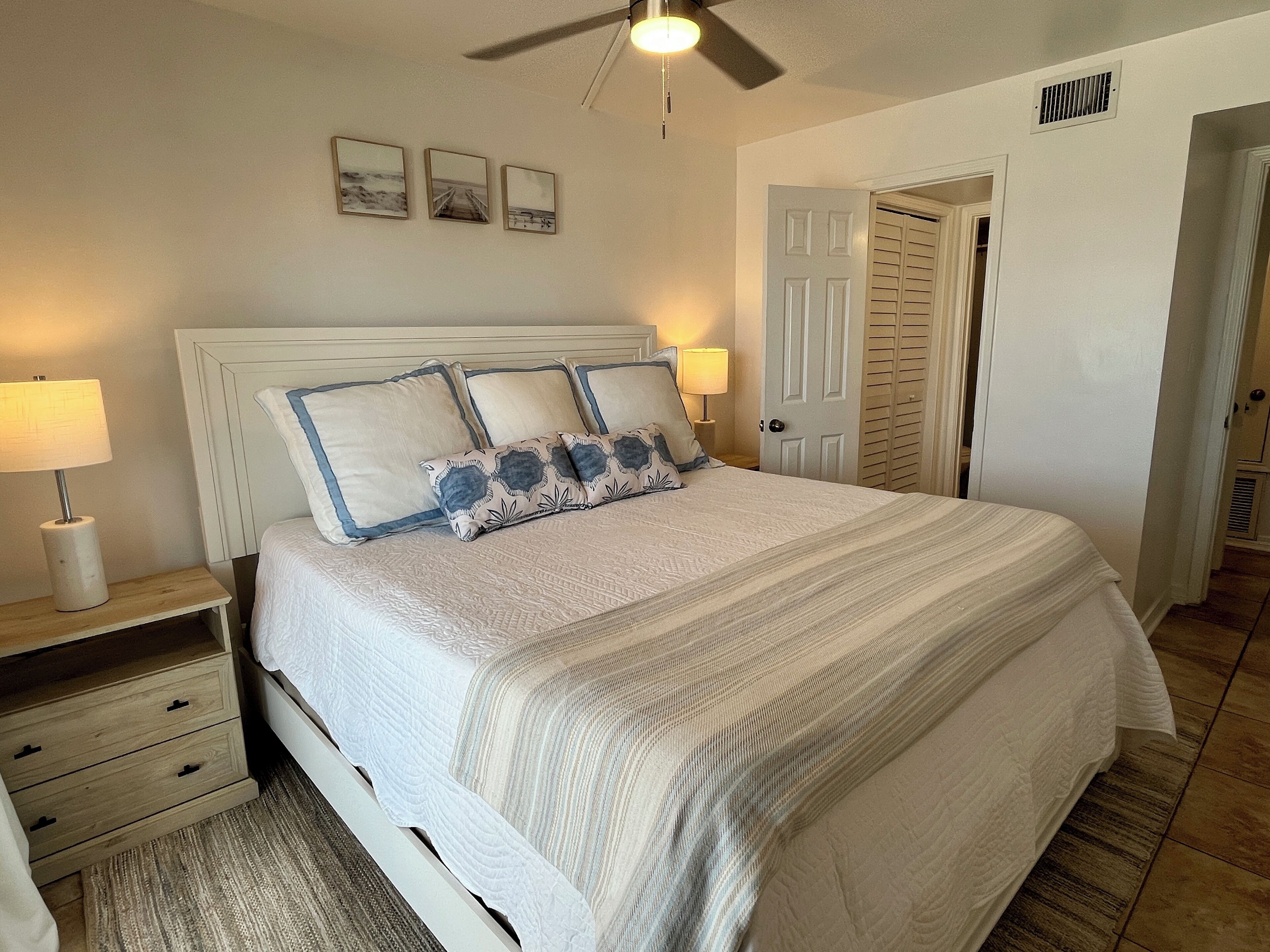Quarto com cama, mesas de cabeceira, ventilador de teto e uma porta.