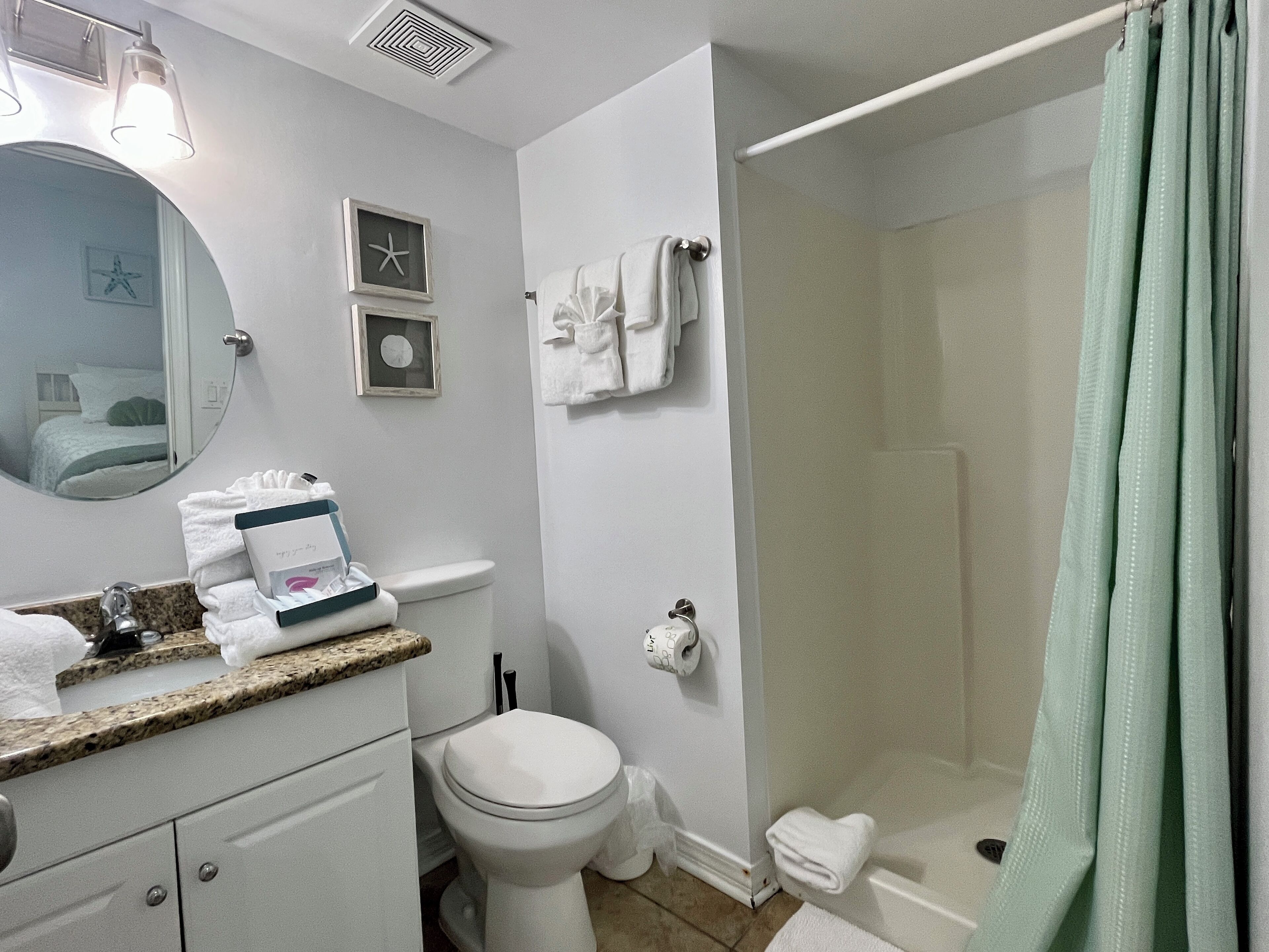 Ein Badezimmer mit Toilette, Waschbecken und Dusche. Auf der Ablage liegen Handtücher und Pflegeprodukte.