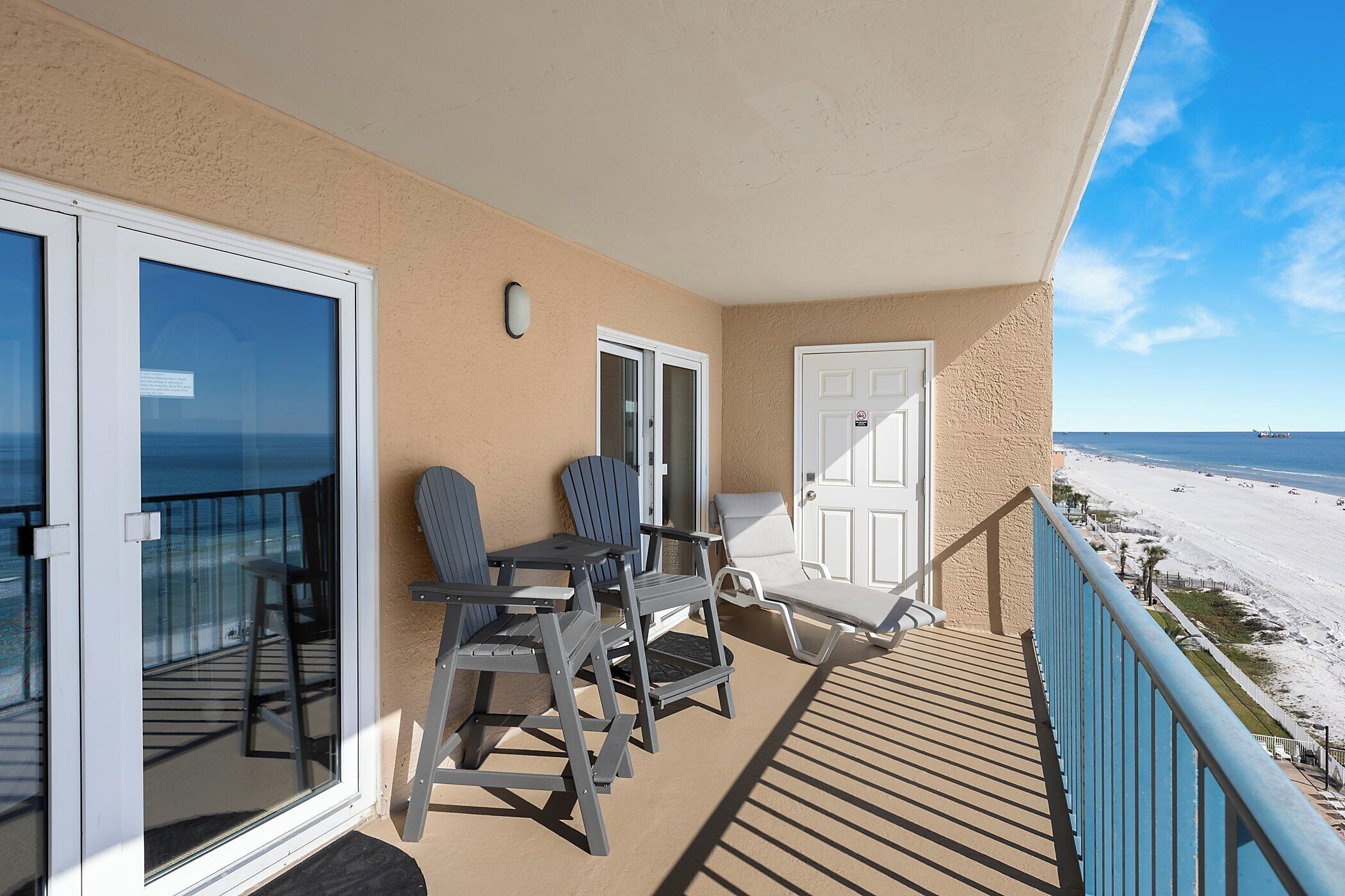 A balcony with a view of the beach, a door, and a chair.