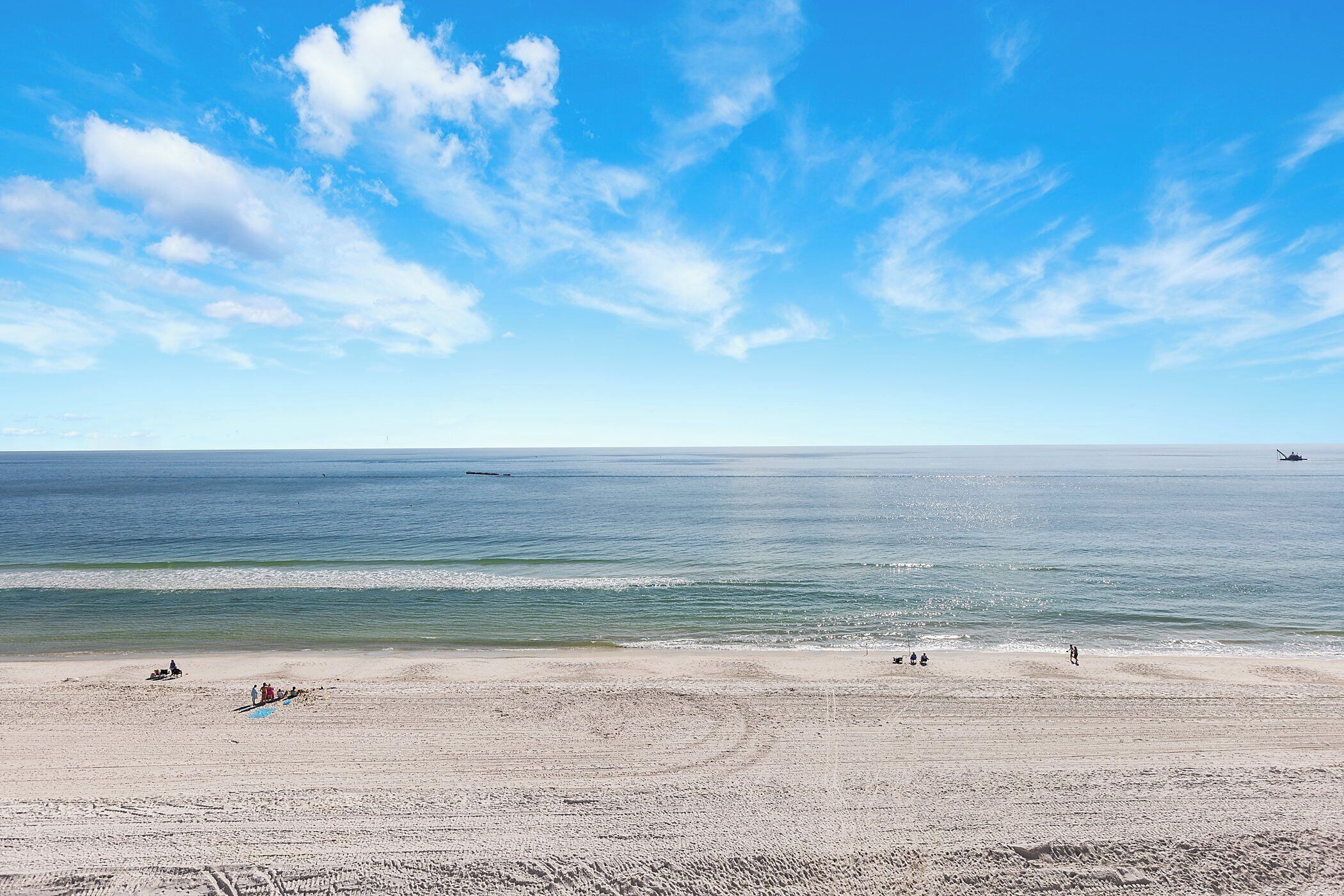 A beach with a clear sky, calm sea, and a few people.
