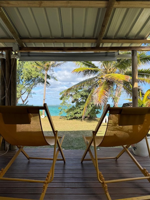 Two yellow lounge chairs facing a beach with palm trees and a clear sky.